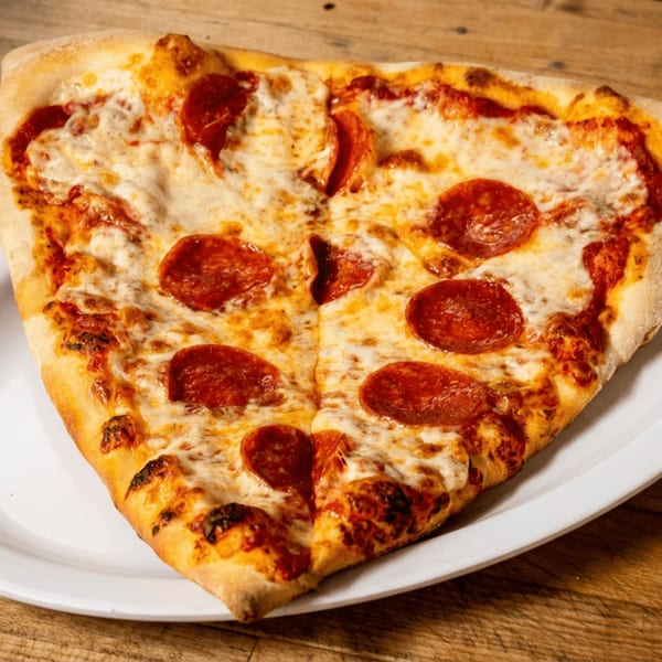 Heart-shaped pepperoni pizza with melted cheese on a white plate atop a rustic wooden table.