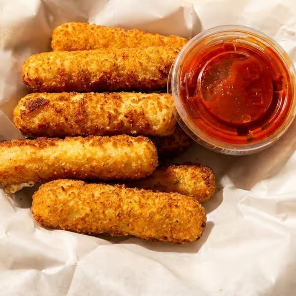Golden-brown breaded mozzarella sticks served with a cup of red marinara dipping sauce.